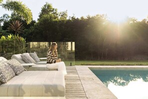 A modern outdoor seating area with a glass partition, a pool, and lush greenery in the background. - The Langville Estate in Kin Kin (Sunshine Coast Hinterland)