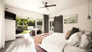 A bedroom with a bed, a ceiling fan, a sliding door to a balcony, and a painting on the wall.