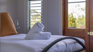 A neatly made bed with a rolled white towel, a brown pillow, and a window with blinds.