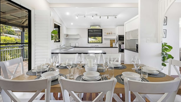 A modern kitchen with white cabinetry, a dining area with white chairs, and a large window overlooking greenery.