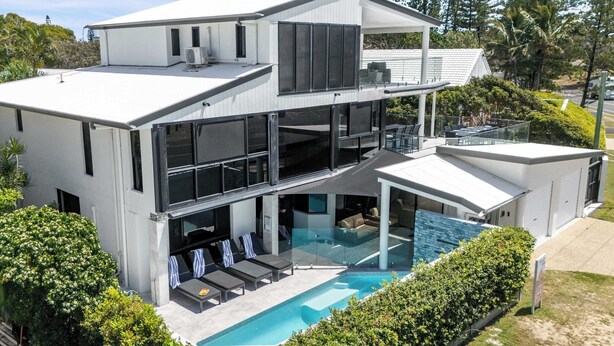 A modern two-story house with a swimming pool, large windows, and a covered outdoor seating area. - Beachfront at Buddina with Heated Pool & Sea Views (Mooloolaba Region)