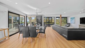 A modern living room with a dining area, large windows, and a black sectional sofa. - Beachfront at Buddina with Heated Pool & Sea Views (Mooloolaba Region)