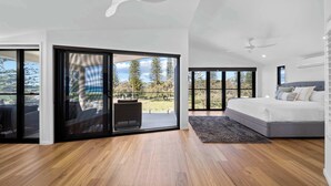 A spacious bedroom with a large bed, a sliding glass door leading to a balcony, and a ceiling fan. - Beachfront at Buddina with Heated Pool & Sea Views (Mooloolaba Region)