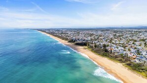 An aerial view of a coastal town with a beachfront, residential buildings, and a clear view of the ocean. - Beachfront at Buddina with Heated Pool & Sea Views (Mooloolaba Region)