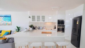 Une cuisine moderne avec des meubles blancs, un îlot central doté de tabourets, un réfrigérateur noir et un four à micro-ondes.