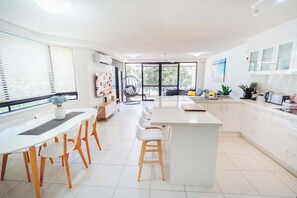 A modern kitchen with a dining area, large windows, and a view of the outdoors. - Picnic Point Waterfront Apartment - Pool & River (Maroochydore Region)