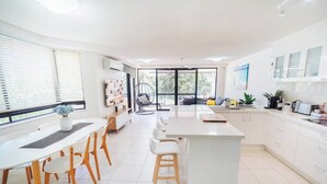 Une cuisine moderne avec des meubles blancs, un îlot central et un coin repas avec des chaises blanches.