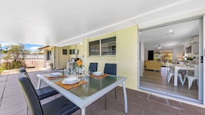 An outdoor dining area with a glass table, chairs, and a view into the house. - Family Home in Maroochydore (Maroochydore Region)