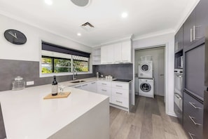 A modern kitchen with a central island, built-in appliances, and a large window. - Family Home in Maroochydore (Maroochydore Region)