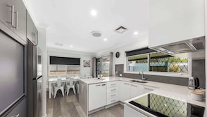 A modern kitchen with a central island, built-in appliances, and a dining area with white chairs. - Family Home in Maroochydore (Maroochydore Region)