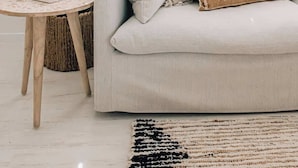 A room with a light-colored sofa, a round wooden side table, a potted plant, and a window with blinds. - Prime location with pool - walk to Coolum Beach (Coolum Region)