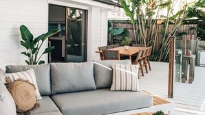 A modern outdoor living space with a grey sectional sofa, a round wooden coffee table, and a dining area with a wooden table and chairs. - Prime location with pool - walk to Coolum Beach (Coolum Region)