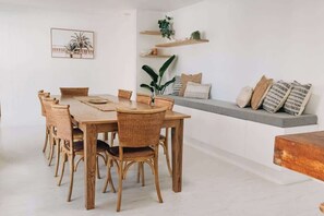 A dining area with a wooden table and chairs, a bench with cushions, and shelves with plants and decorative items.