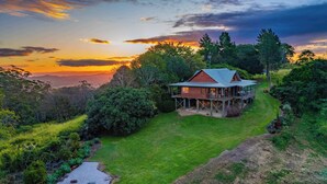 Uma casa com varanda, rodeada por vegetação exuberante e uma vista panorâmica do pôr do sol.