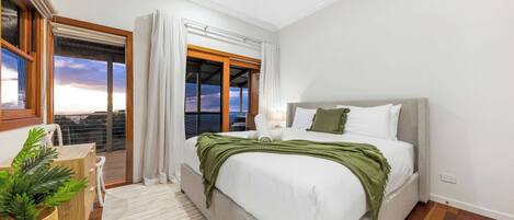 Une chambre à coucher avec un lit, un bureau, une chaise, une plante et une vue sur le ciel par la fenêtre.