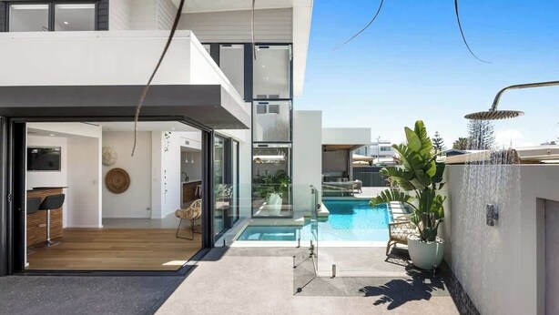 Une maison moderne à deux étages, dotée d’un patio entièrement vitré, d’une piscine et d’une grande plante en pot.