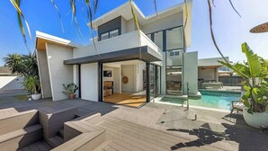 Une maison moderne dotée d’une piscine, d’un espace salon extérieur et d’un escalier menant à l’entrée.