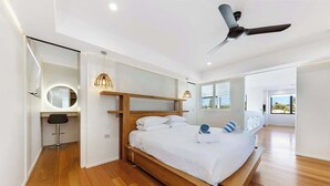 Une chambre à coucher moderne avec un lit en bois, un ventilateur de plafond et un miroir rond.