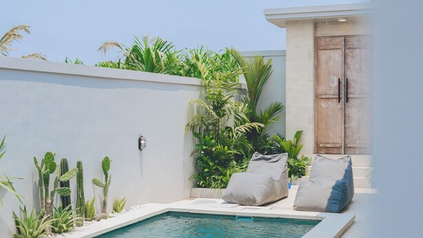 A swimming pool with a white tiled deck, surrounded by cacti and plants, and a wooden door in the background. - Santai Villa by Betterplace (Kerobokan)