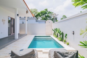 Une piscine avec une terrasse carrelée, deux chaises longues et un mur végétalisé.