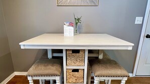 Una mesa blanca con dos bancos acolchados, un adorno en la pared y un pequeño jarrón con una planta.
