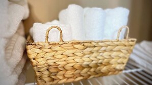 Una cesta tejida con asas que contiene toallas blancas, colocada sobre un estante.