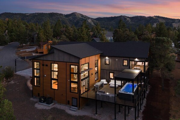 Una casa moderna de dos pisos con un balcón y jacuzzi, rodeada de un paisaje boscoso.