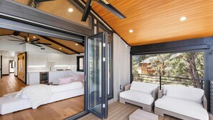 Un interior moderno con un amplio ventanal corredera que da a un balcón, una zona de estar acogedora con sofás blancos y una cocina a la vista.