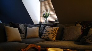 A cozy living room with a sectional sofa, a small side table with a vase, and a window with blinds. - Georgianstyle-2bed-smarttv-freeparking (Boston)