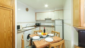 A compact kitchen with wooden cabinets, a microwave, a sink, a washing machine, and a dining table set with plates, glasses, and a bowl of fruit. - Comtessa in Oliva With 1 Bedrooms and 1 Bathrooms (Oliva)