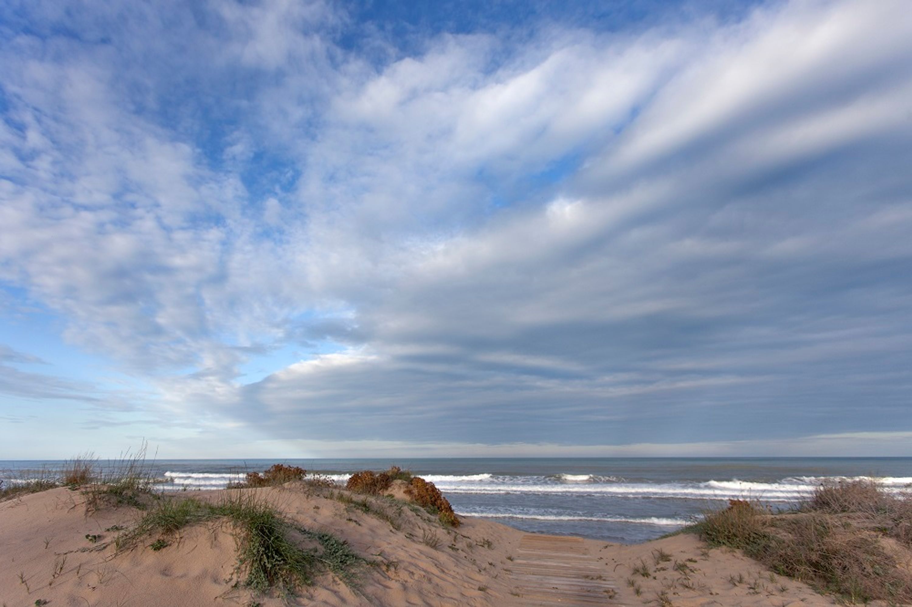 Une plage avec des dunes, une promenade en bois et l’océan.