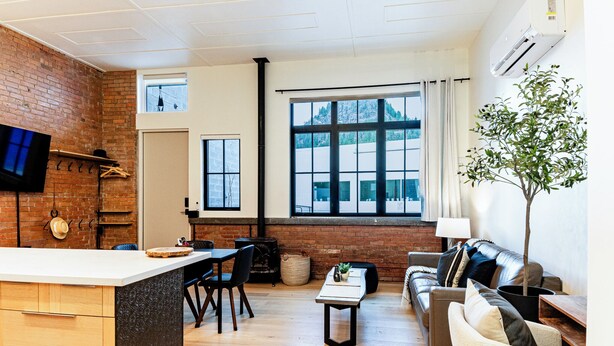 A modern living room with a kitchen area, large windows, a flat-screen TV, and a potted plant. - Retro Vibe,  downtown Grand Forks (Grand Forks)
