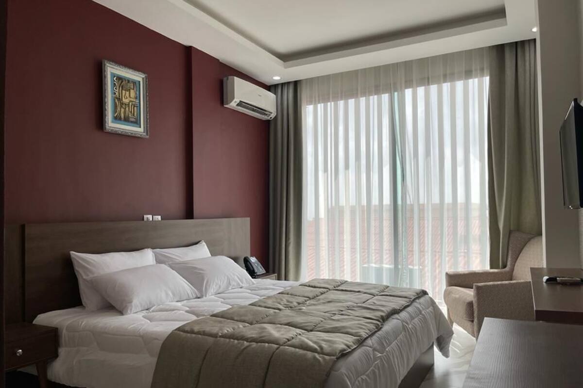 A hotel room with a large bed, a desk, a chair, and a window with curtains.