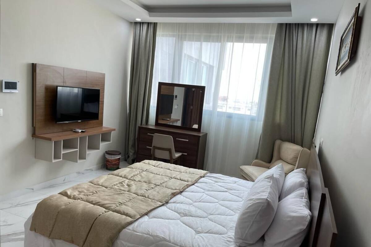 A hotel room with a bed, a TV, a desk, a chair, and a large window with curtains.