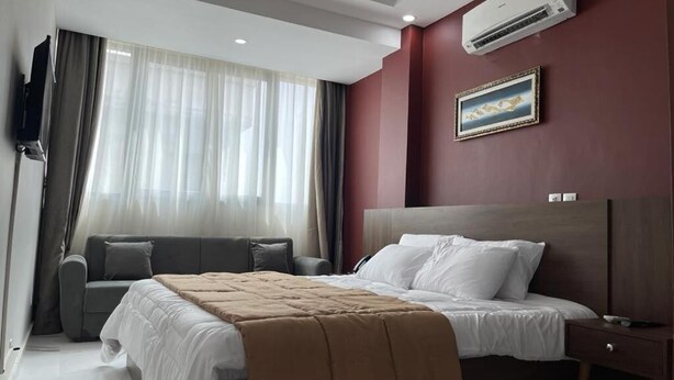 A hotel room with a bed, a sofa, a TV, and an air conditioner. - RESIDENCE SYCOMORE 1 (Abidjan)