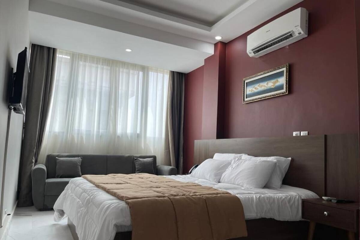 A hotel room with a bed, a sofa, a TV, and an air conditioner.