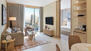 Una habitación de hotel moderna con sofá, sillón, mesa de centro y televisión.