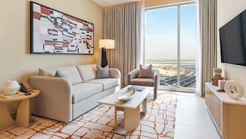 A modern hotel room with a sofa, armchair, and a coffee table. There is a large window with a view of a cityscape.