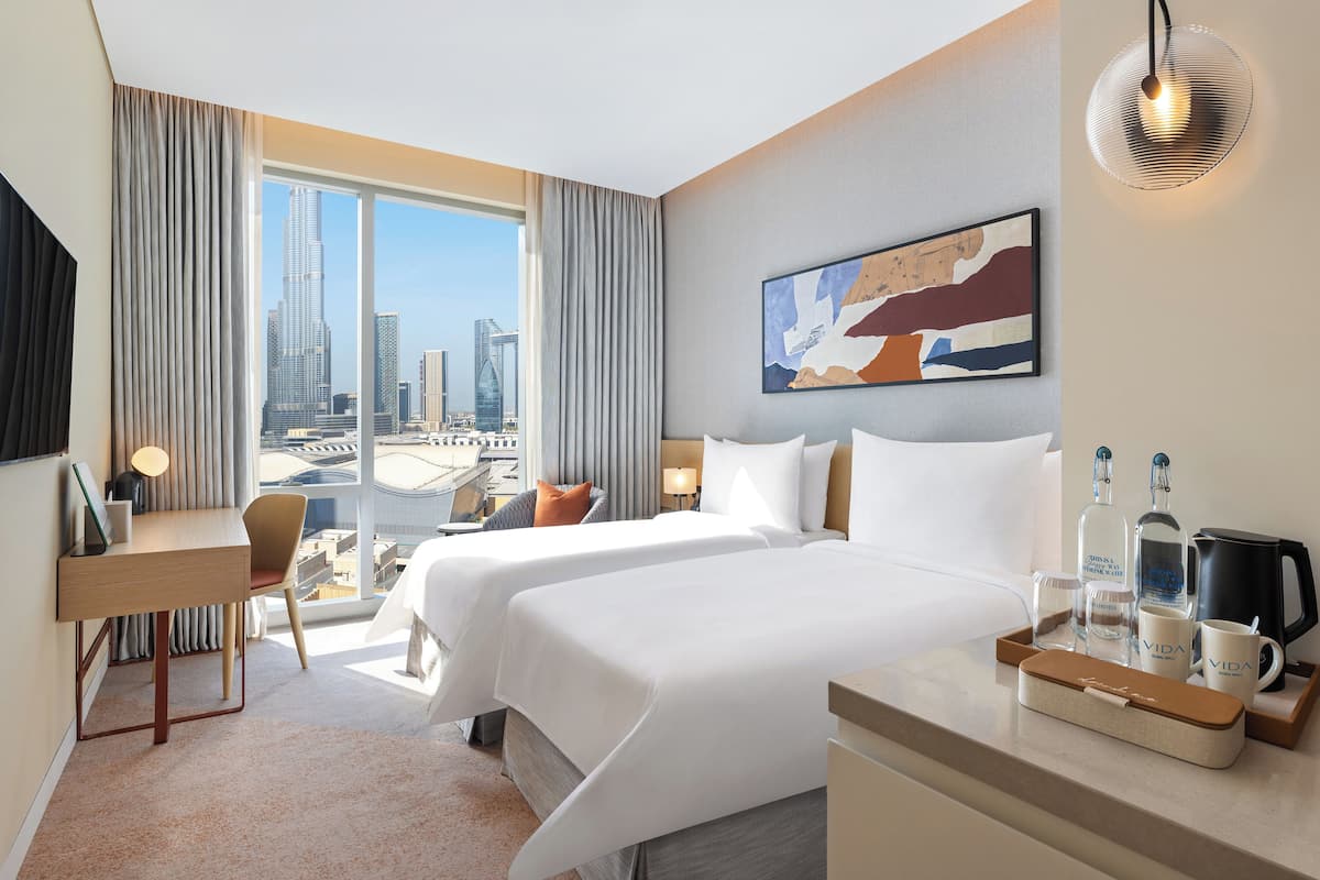 A hotel room with two beds, a desk, a chair, a coffee maker, and a tray with bottles and cups.