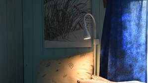 Une chambre à coucher avec un lit, des oreillers, une lampe fixée au mur et un tableau encadré.