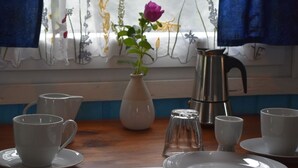 Une table à manger dressée avec des tasses et des soucoupes blanches, un vase blanc contenant une fleur violette, un pichet en métal et un salier.