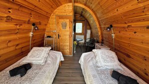Acogedora habitación tipo cabaña de madera con dos camas, un pequeño rincón americano y techo de madera.