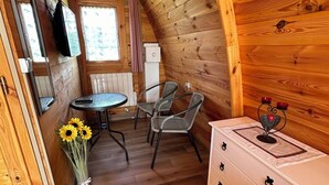 Interior acogedor de una cabaña de madera con comedor, un aparador blanco y una ventana con cortinas.
