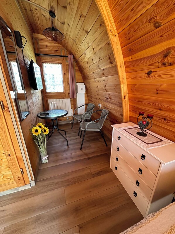 A cozy wooden cabin interior with a dining area, a white dresser, and a window with curtains.
