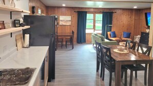 A modern kitchen with a refrigerator, wooden cabinets, and a dining area with a table and chairs. - Walk to the Concerts! (Arnolds Park)