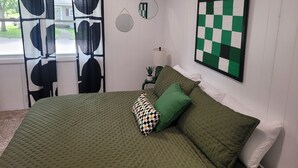 A bedroom with a large bed, green bedding, a checkered wall art piece, and a window with curtains. - Walk to the Concerts! (Arnolds Park)