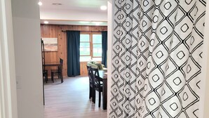 A room with a wooden floor, a dining area with a table and chairs, and a patterned curtain. - Walk to the Concerts! (Arnolds Park)