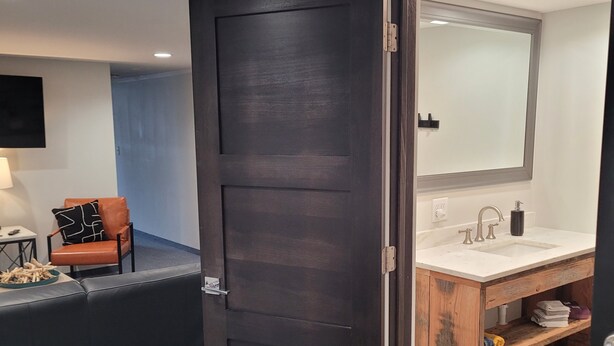 Een moderne badkamer met een houten wastafelmeubel, een grote spiegel en een donkere houten deur.