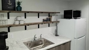 Een keuken met een spoelbak, een magnetron en planken met mokken en een plant.