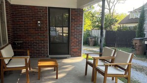 A covered patio with four wooden chairs and a bench, brick walls, and a sliding glass door. - This house is a 2 bedroom(s), 1 bathrooms, located in Nashville, TN. (Nashville)